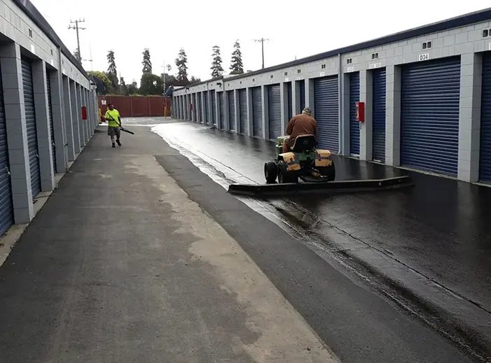 A man riding a scooter down the street near storage units.